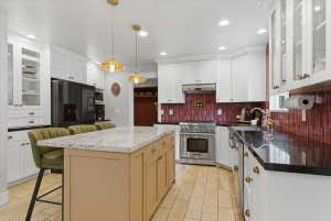 Spacious kitchen featuring a large island with a two-toned countertop, white cabinetry, steel appliances, and tile flooring