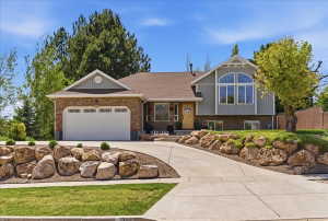 Multi-level residence featuring a two-car garage with exterior lighting, a stone facade