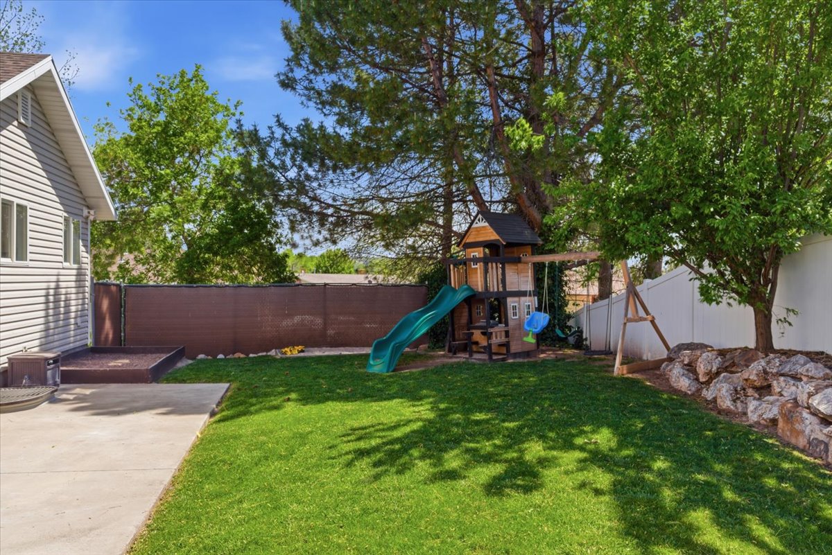 Expansive backyard featuring a lush lawn, concrete patio, playground and mature trees