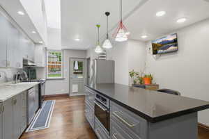 Modern kitchen featuring an expansive center island with an integrated oven, dark solid-surface countertop, and pendant lighting