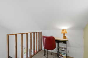 Carpeted loft area featuring a natural wood railing and white walls
