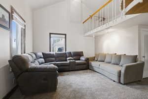 Living area featuring vaulted ceilings, a carpeted floor, and multiple windows with dark wood trim