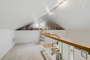 Carpeted loft area featuring a curved staircase with wood handrails and white balusters, track lighting, and an additional elevated platform