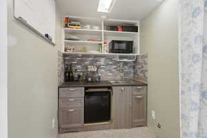 Compact wet bar featuring a built-in sink, under-counter refrigerator, tile backsplash, and open shelving