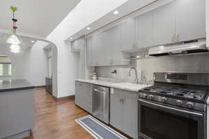 Kitchen featuring light gray cabinetry with gold-tone hardware, stainless steel appliances, and wood-finish flooring