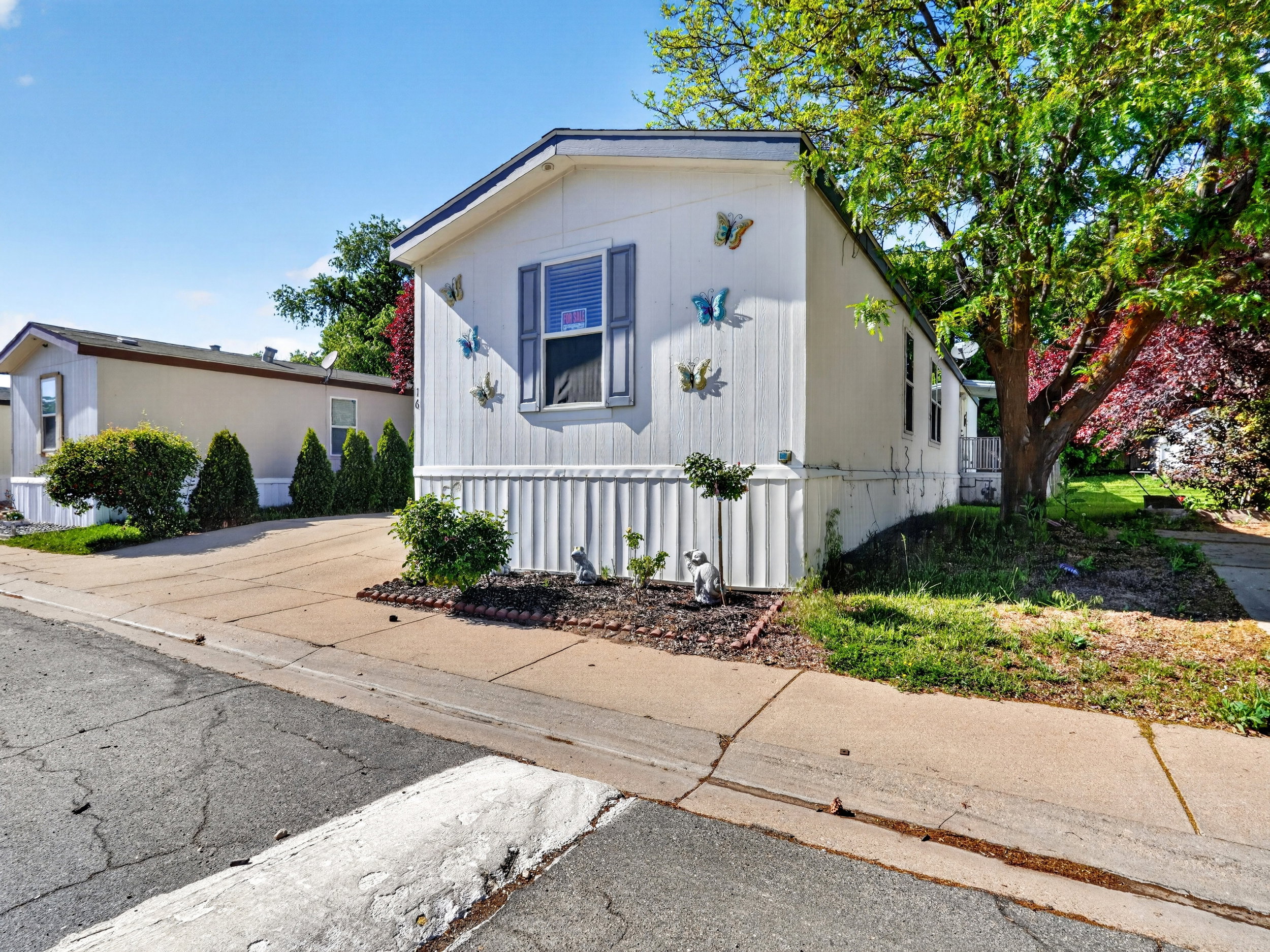 White exterior siding with vertical accents, dark shutters, and a landscaped bed with dark mulch and small shrubs