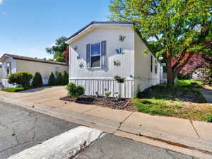 White exterior siding with vertical accents, dark shutters, and a landscaped bed with dark mulch and small shrubs