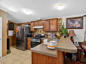 Kitchen featuring wood cabinetry, a stainless steel refrigerator, and a gas range with an overhead vent