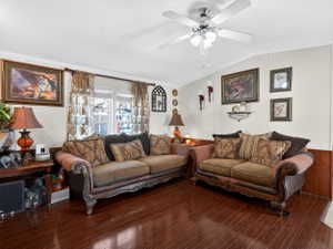 Living area featuring wood-finish flooring, white walls with wood wainscoting, a ceiling fan with integrated lighting, and a double window with blinds