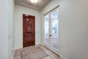 Entryway featuring a wood-panel door, decorative tile flooring, and a tray ceiling with a flush-mount light fixture