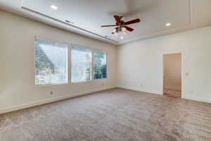 Spacious interior room featuring plush carpet flooring, recessed lighting, a ceiling fan with light kit, a tray ceiling, and multiple windows with horizontal blinds