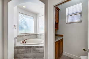 Corner soaking tub with a tiled surround, recessed lighting, and dual windows with blinds