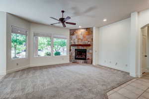 Spacious interior featuring a stone-clad fireplace with a wood mantel, overhead ceiling fan, recessed lighting, and multiple windows