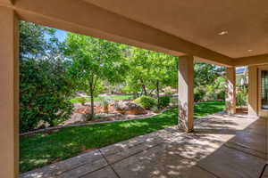 Expansive covered patio with recessed lighting overlooking a landscaped yard featuring mature trees, green lawn, and decorative rock elements