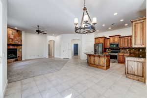 Open-concept area featuring a kitchen with wood cabinetry and stainless steel appliances, a central island with a solid surface countertop, and a living area with a stone-clad fireplace