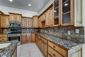 Kitchen featuring light wood cabinetry, speckled granite countertops, a tiled backsplash, stainless steel appliances, and recessed lighting