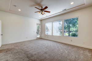 Spacious room featuring neutral carpeting, a ceiling fan with integrated lighting, recessed lighting, and a tray ceiling