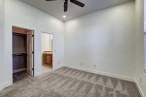 Spacious room featuring neutral carpeting, a ceiling fan, recessed lighting, a walk-in closet with built-in shelving, and an en-suite bathroom with a wood-finish vanity