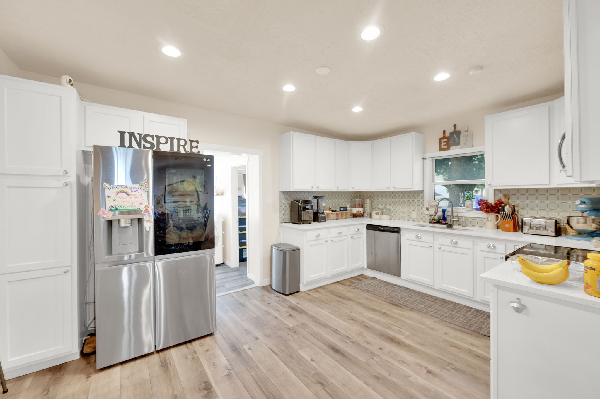 Bright kitchen featuring white cabinetry, wood-finish flooring, recessed lighting, and a patterned tile backsplash