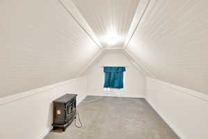 Attic space featuring vaulted ceilings with beadboard paneling, neutral carpeting, and a single window