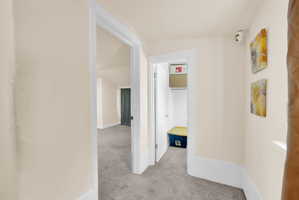 Hallway with neutral wall tones, white trim, and gray carpeted flooring