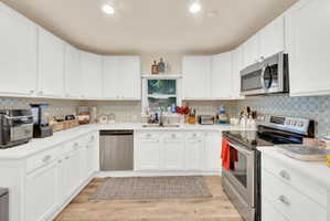 Kitchen featuring extensive white cabinetry, light countertops, wood-finish flooring, stainless steel appliances, and a tiled backsplash