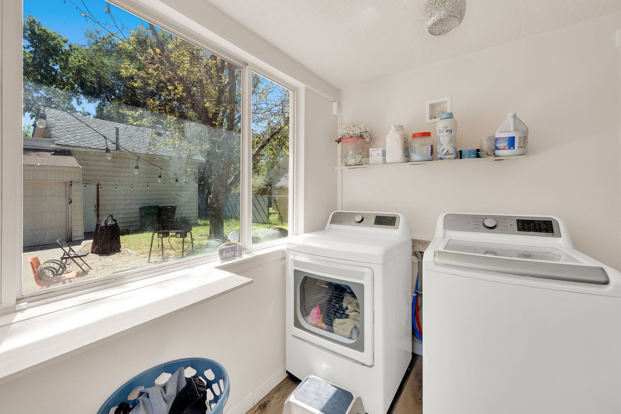 Bright laundry area featuring a large window, white walls, and wood-finish flooring