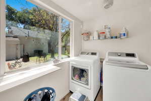 Bright laundry area featuring a large window, white walls, and wood-finish flooring
