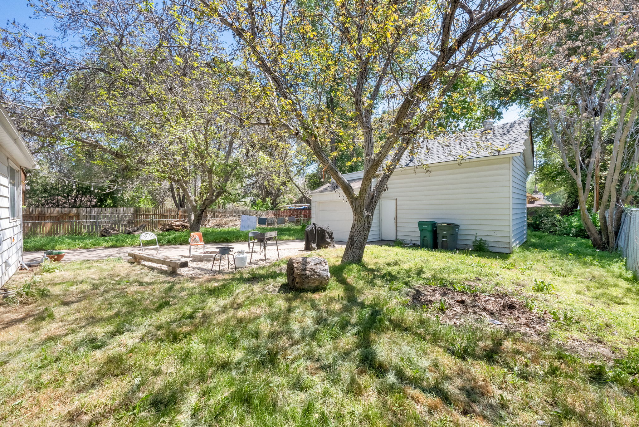 Expansive backyard featuring a detached garage with horizontal siding, mature deciduous trees, a concrete patio area, and perimeter fencing