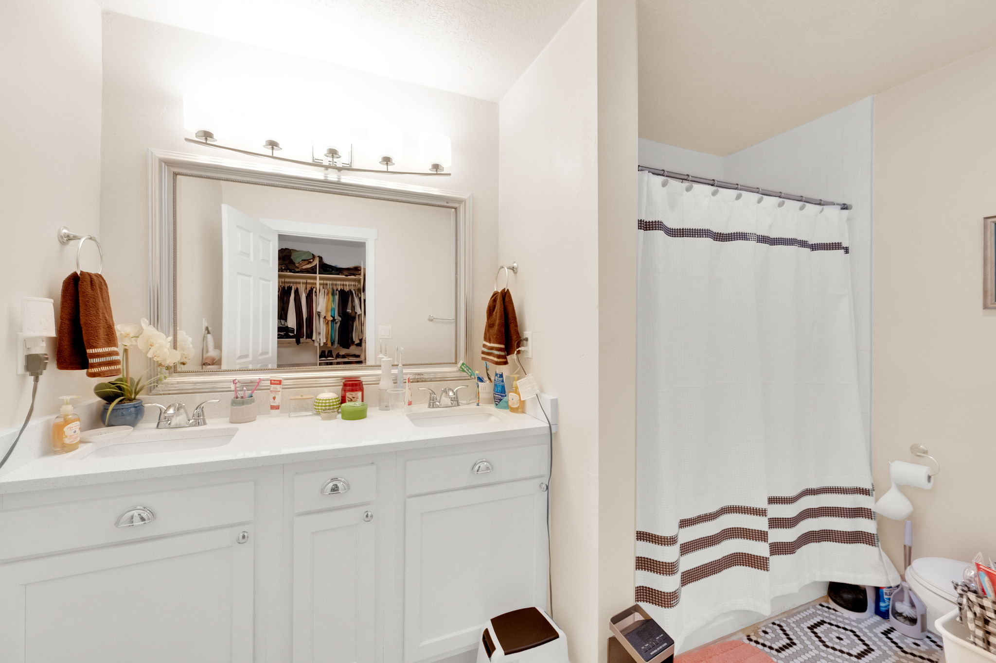 Dual vanity with chrome fixtures and ample counter space, complemented by a large framed mirror with overhead lighting
