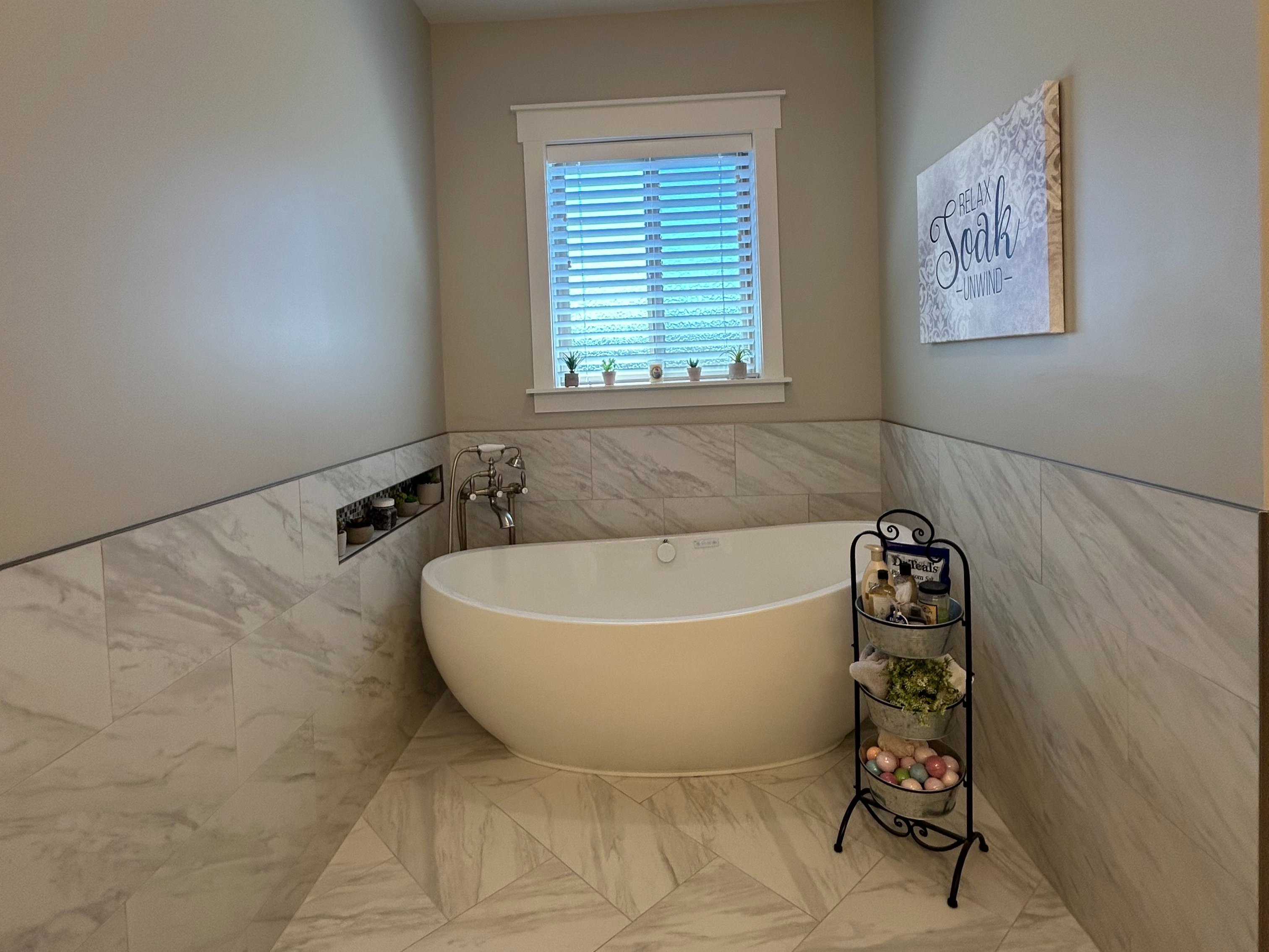Freestanding soaking tub with floor-mounted faucet, complemented by wall-to-ceiling tile in a neutral tone