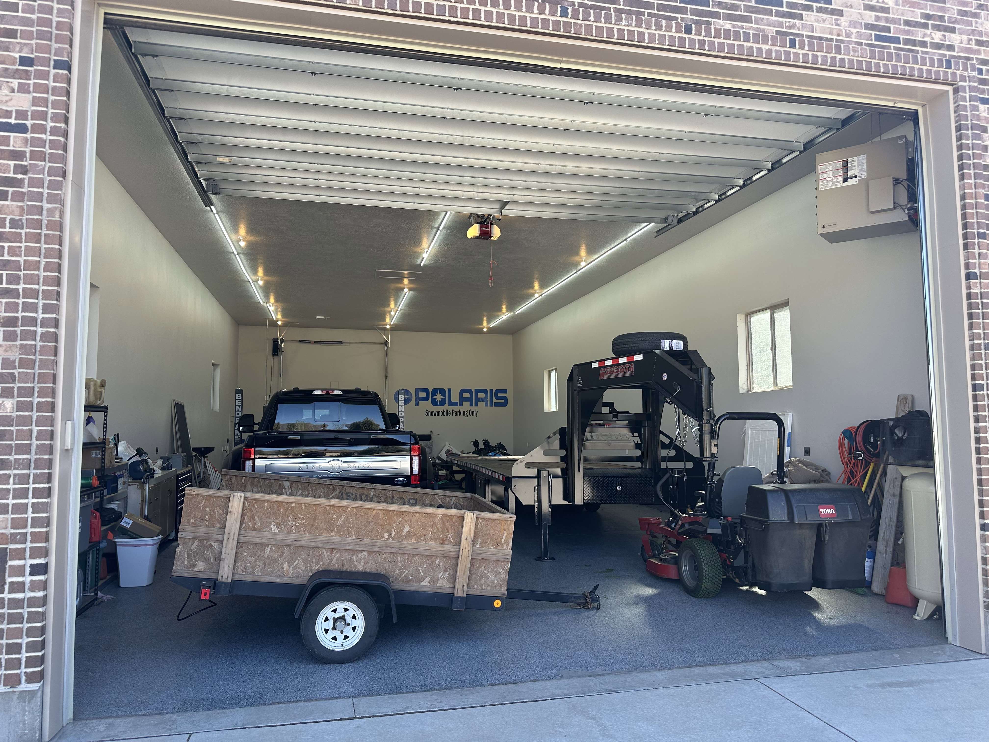 Spacious garage featuring a brick exterior, multiple strip lighting fixtures, a large overhead door, and two side windows