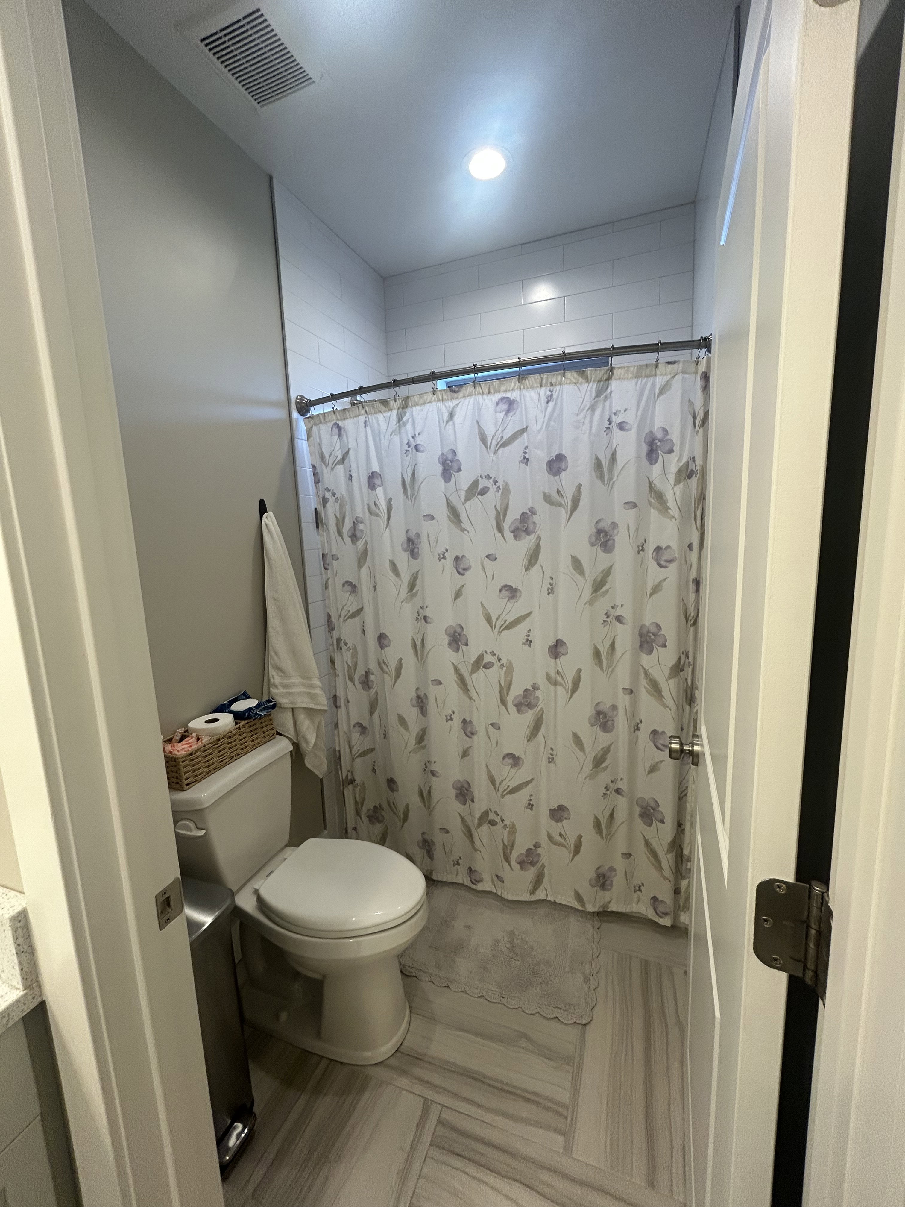 Bathroom featuring a walk-in shower with white subway tile, a white toilet, and wood-finish flooring in a herringbone pattern