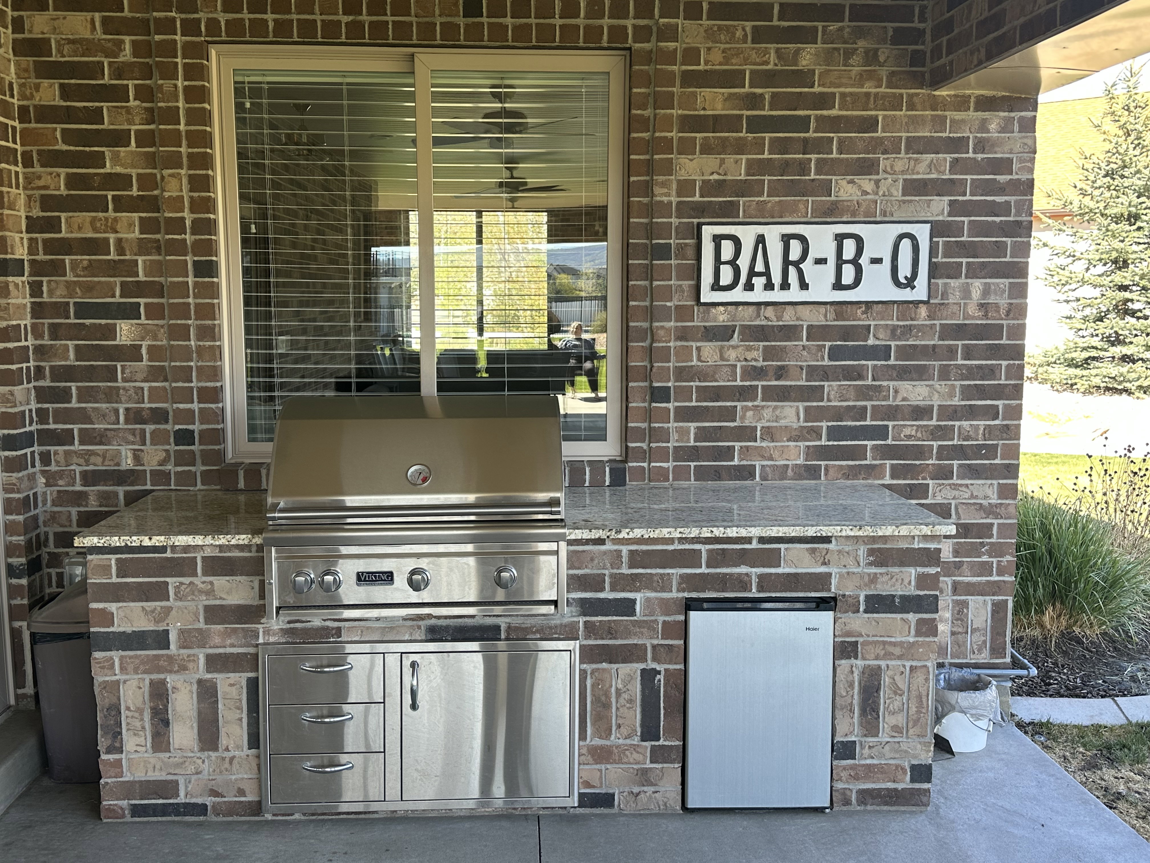 Outdoor kitchen featuring a built-in stainless steel grill, integrated storage drawers, and a compact refrigerator