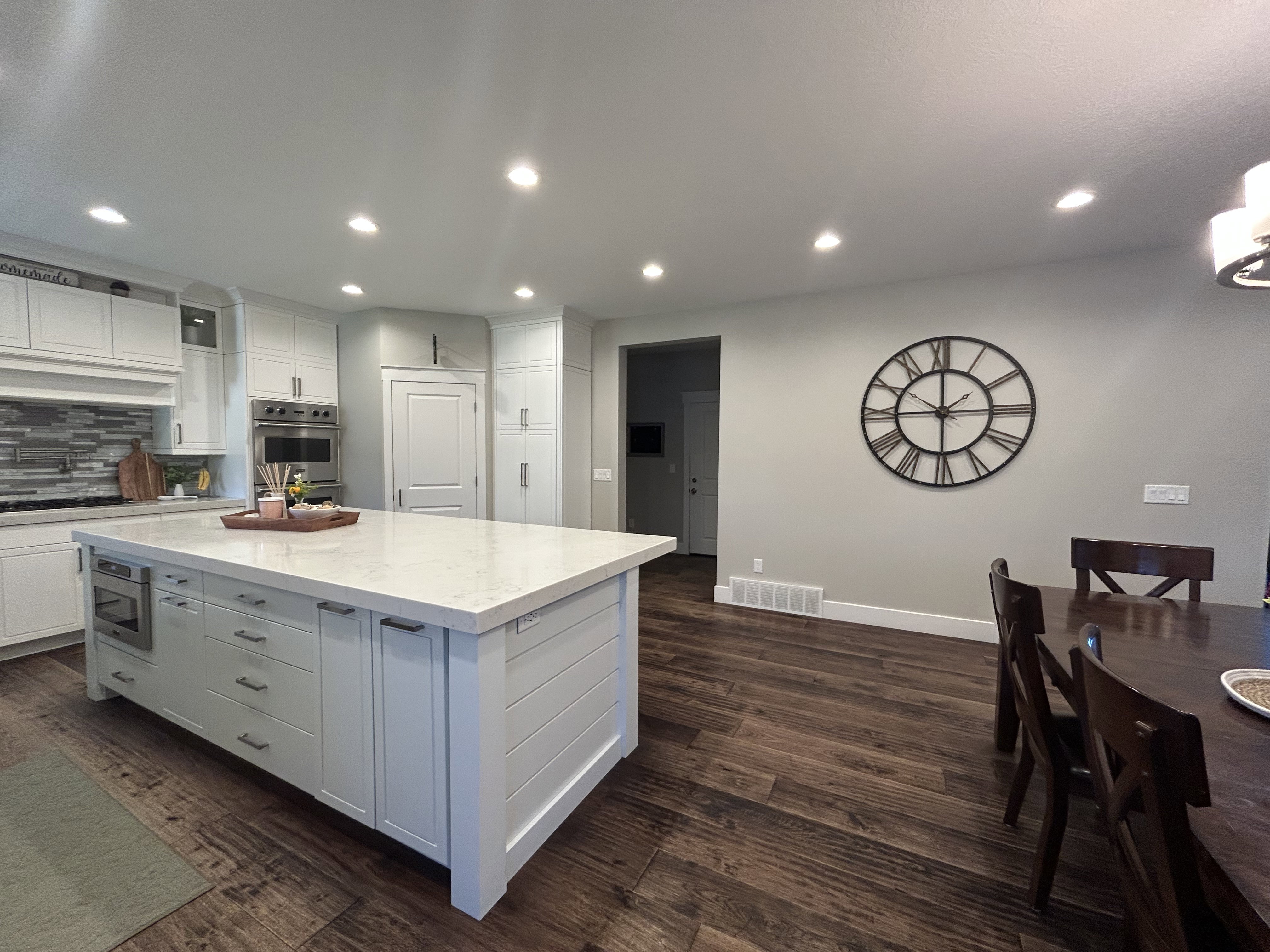 Gourmet kitchen featuring a large island with a light-toned countertop, stainless steel appliances, extensive white cabinetry, and wood-finish flooring