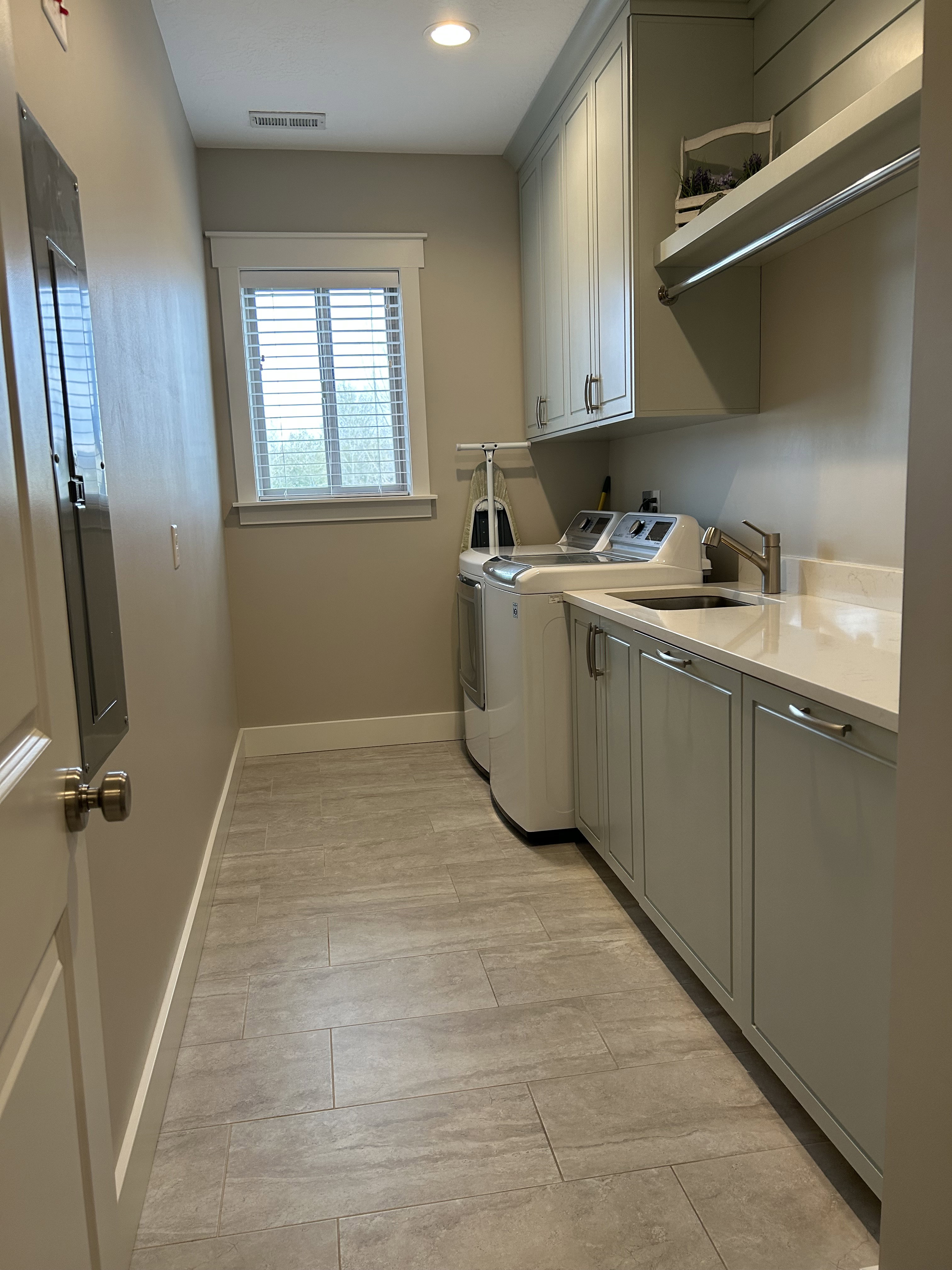Laundry room featuring light gray cabinetry, a built-in sink with a gooseneck faucet, light countertops, and plank-style floor tiling