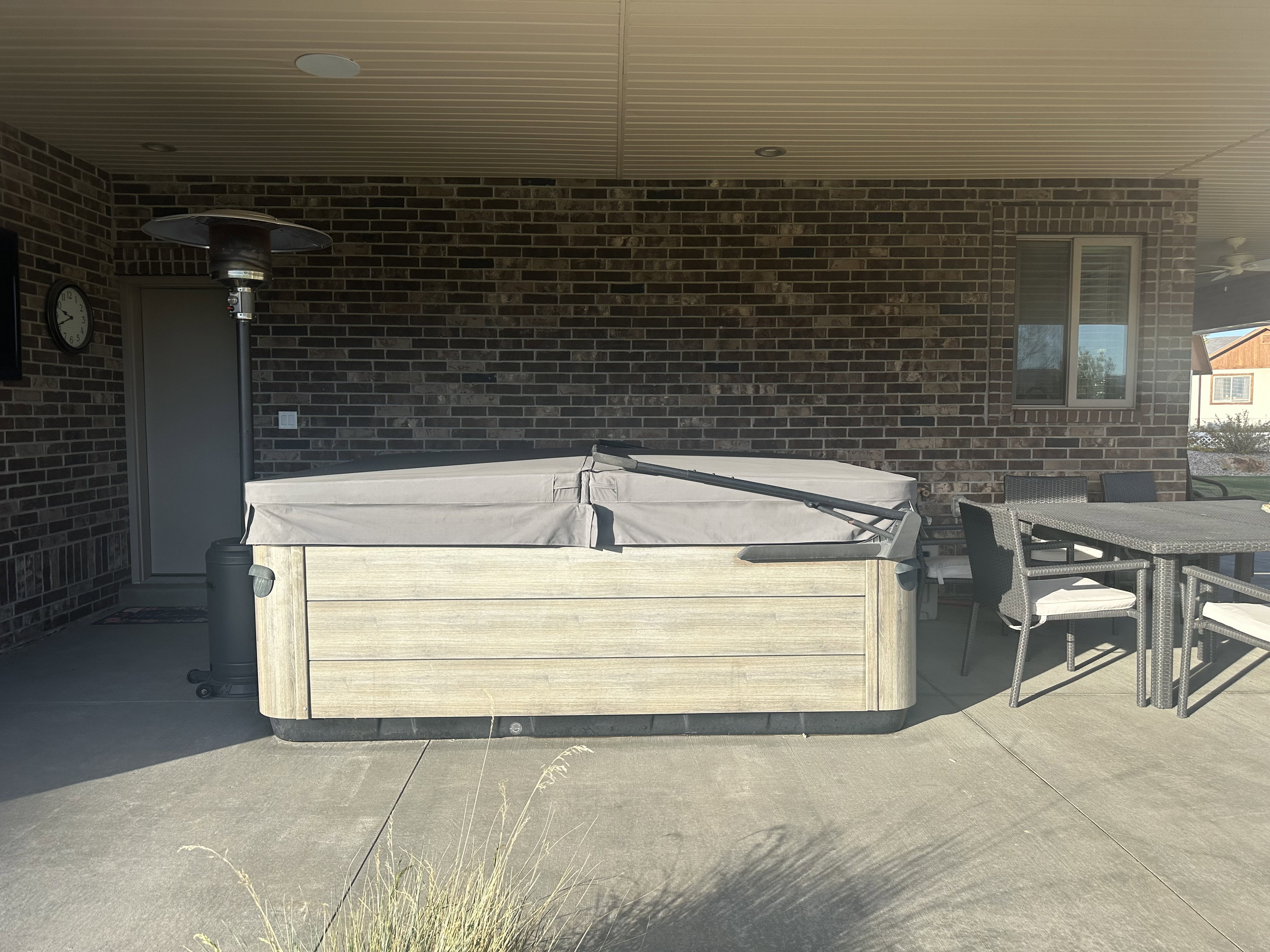 Covered patio featuring a hot tub with a light wood-finish exterior, concrete flooring, and a brick exterior wall