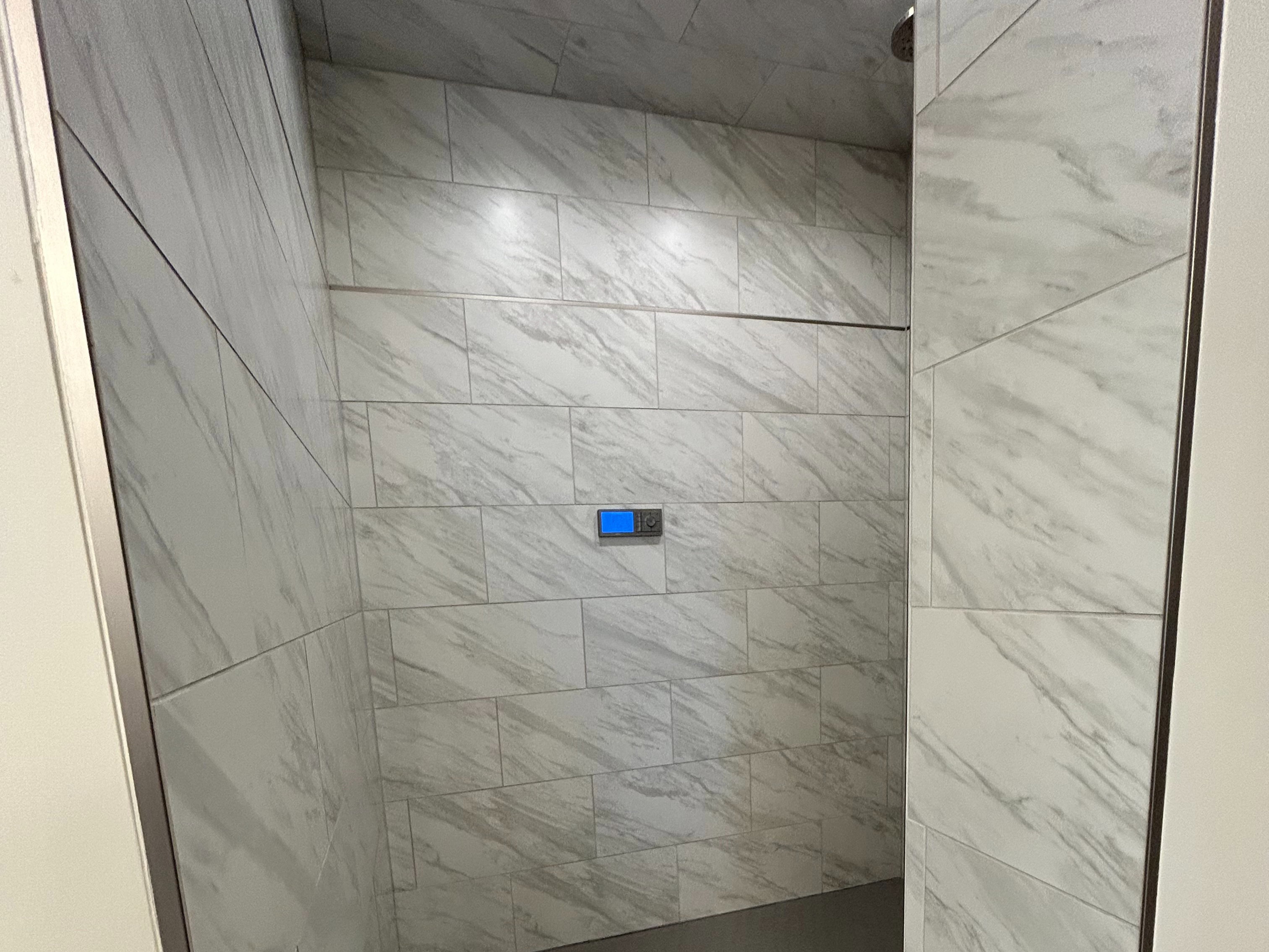 Walk-in shower featuring light-toned large format wall tiling, a dark hexagonal tile floor, recessed lighting, and a digital shower control panel