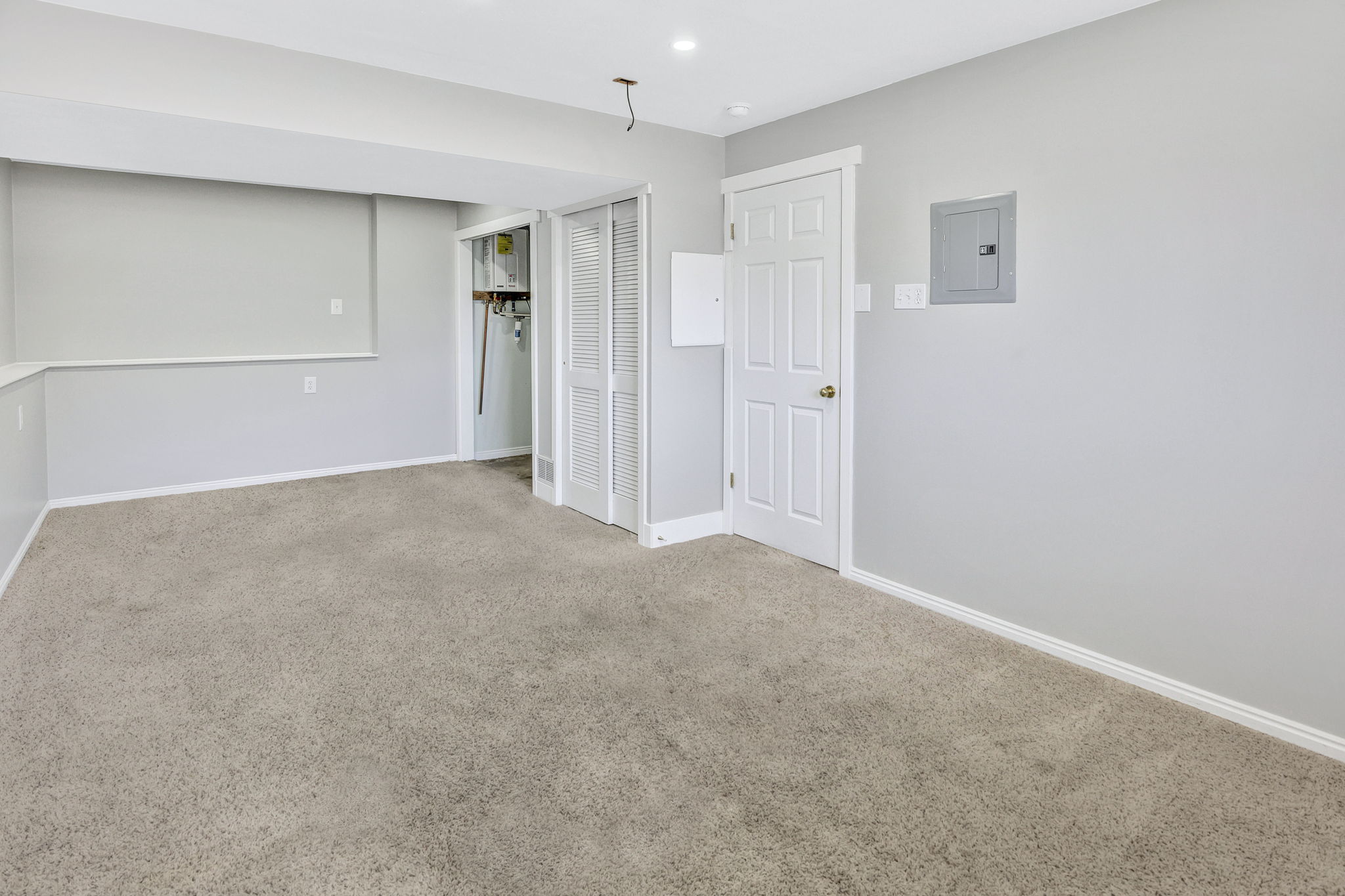 Spacious room with light gray walls, plush carpeting, white trim, and recessed lighting
