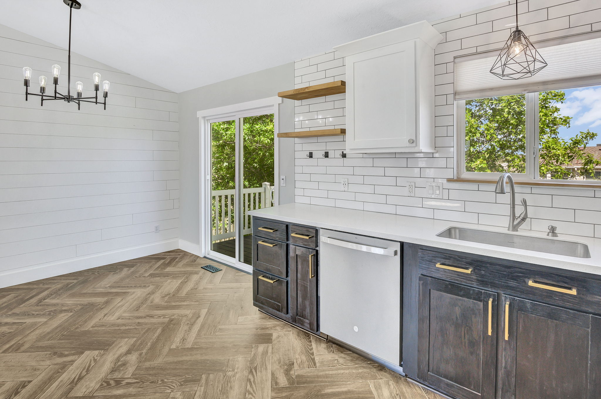 Open-concept kitchen and dining area featuring herringbone wood-finish flooring, white shiplap accent wall, and a contemporary chandelier