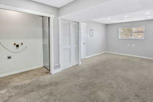 Carpeted interior space with a window, recessed lighting, white louvered bifold doors, and a laundry hookup area with a concrete floor