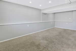 Spacious room featuring neutral carpeting, light gray wall paint, white trim, recessed lighting, and a drop ceiling with integrated lighting