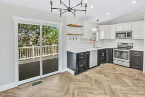 Kitchen featuring black and white cabinetry, a white subway tile backsplash, stainless steel appliances, and wood-finish herringbone flooring