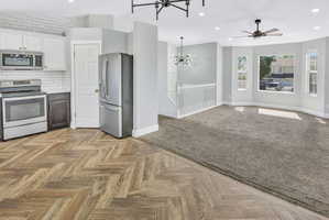 Kitchen with wood-finish flooring in a herringbone pattern, stainless steel appliances, white cabinetry, and subway tile backsplash