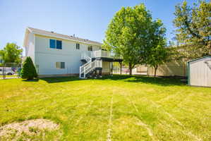 Spacious backyard featuring a two-story residence with light-colored siding, a second-story deck with white railings, and mature trees providing shade