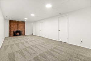 Spacious room featuring a brick fireplace with a black metal grate, light-toned patterned carpeting, white painted walls, and recessed lighting