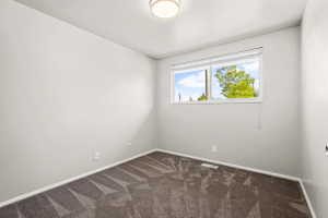 Room featuring a window with white blinds, light gray walls, dark patterned carpeting, and white baseboards