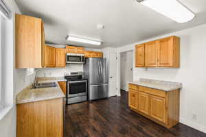 Kitchen featuring wood-finish cabinetry, stainless steel appliances, speckled countertops, and dark wood-finish flooring