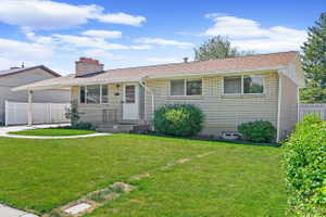 Single-story residence featuring light-colored brick siding, a brown shingle roof, an attached carport, a front porch with an iron railing, and a manicured lawn with mature landscaping
