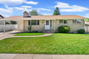 Brick exterior with a peaked roofline, featuring a covered carport, established front landscaping, and a concrete driveway